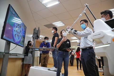 CUBA ROBOTIK: Menteri Kesihatan, Encik Ong Ye Kung (dua dari kanan) sedang mencuba ArmMotus EMU, iaitu robot yang direka khas untuk pemulihan semula bahagian anggota tubuh atas dalam lawatannya ke Cart semalam.- Foto-foto BH oleh KEVIN LIM