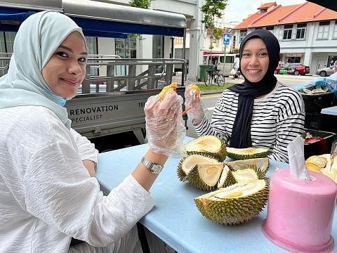 HARGA DURIAN TURUN: (dari kiri) Cik Shaakira dan Cik Dzulhijjah mengambil kesempatan harga murah durian dan menjamu selera di sebuah kedai durian di Geylang Lorong 36. - Foto BH oleh HAKIM YUSOF