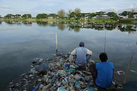 PENCEMARAN TERUK: Dua lelaki yang memancing kelihatan duduk di atas timbunan sampah plastik di sebuah kolam ikan di Aceh, Indonesia. - Foto AFP