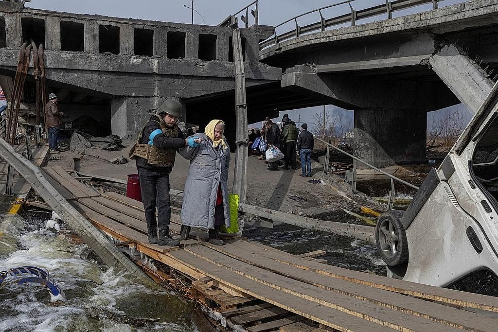 MUSNAH: Seorang anggota tentera Ukraine membantu wanita meninggalkan bandar Irpin, berdekatan ibu kota Kyiv, yang teruk dibedil tentera Russia. - Foto REUTERS