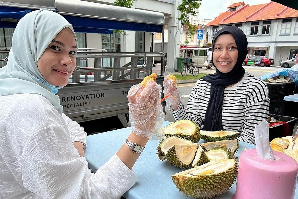 HARGA DURIAN TURUN: (dari kiri) Cik Shaakira dan Cik Dzulhijjah mengambil kesempatan harga murah durian dan menjamu selera di sebuah kedai durian di Geylang Lorong 36. - Foto BH oleh HAKIM YUSOF
