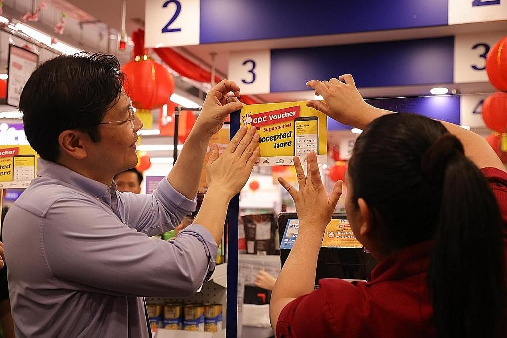 BAUCAR CDC: Encik Wong bersama seorang kakitangan pasar raya NTUC FairPrice cawangan Kampong Admiralty menampalkan pelekat Baucar CDC 2023 berwarna kuning sempena pelancarannya semalam. - Foto BH oleh ONG WEE JIN